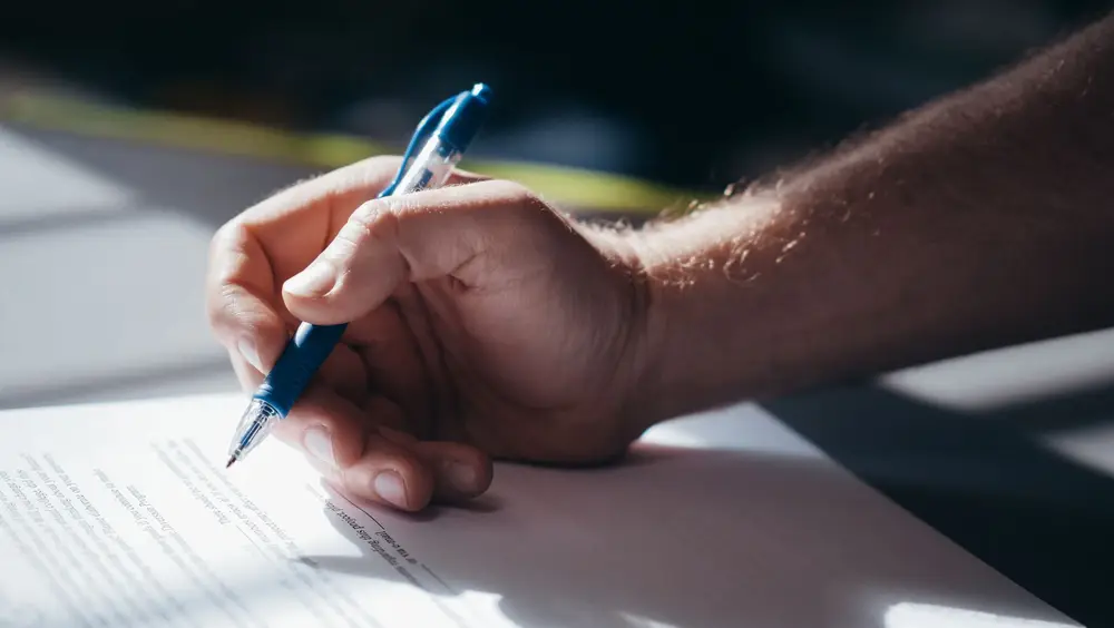 A hand signing a document with a blue pen